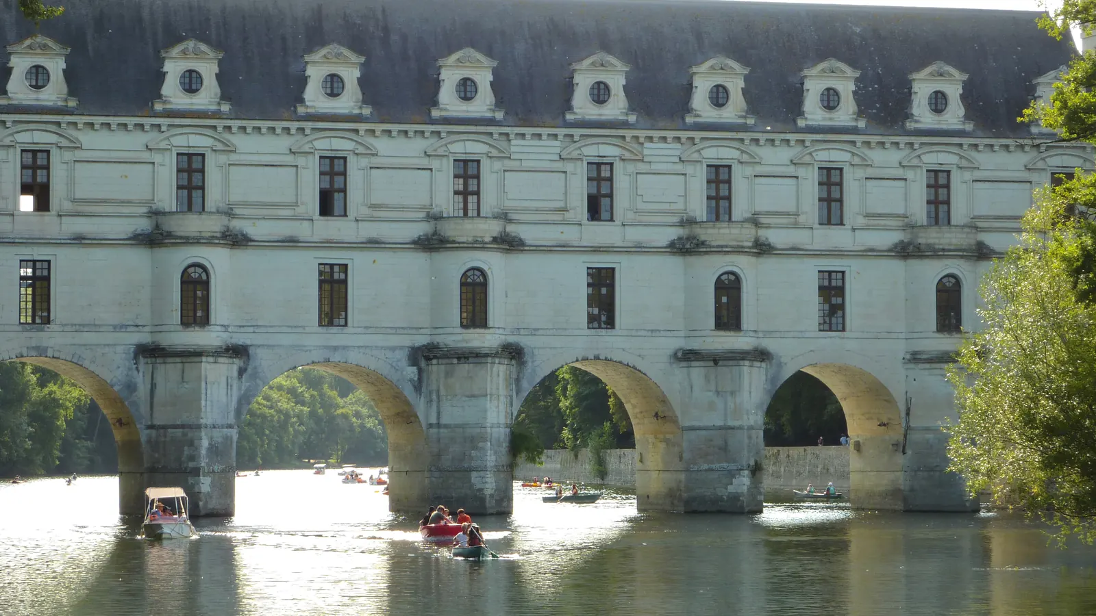 Les arches de pierre du château de Chenonceau à contre-jour au-dessus du Cher, des canoës passent en dessous.