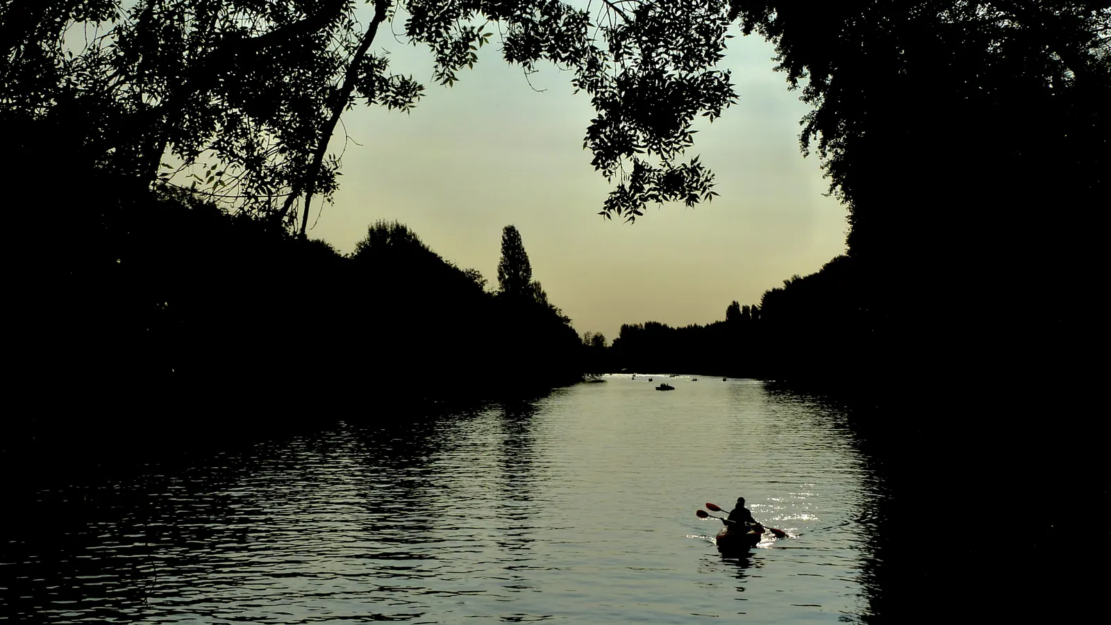 Un kayak en silhouette sur le Cher au crépuscule, entre deux rives sombres.